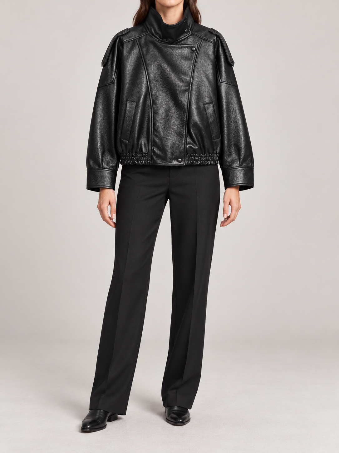 black cropped leather-look bomber with tall stand collar, asymmetric snap front, dropped shoulders and elasticated hem, front view on a model