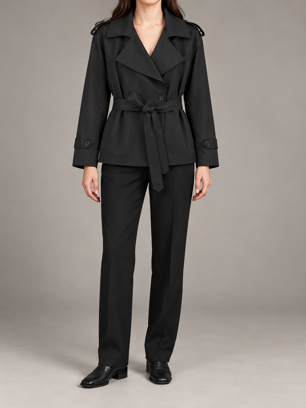 black double-breasted short trench with wide V-neck lapels, waist tie and buttoned cuff tabs, front view on a model